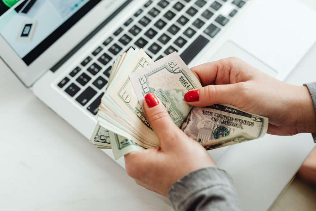 Woman counting American money while laptop in the background