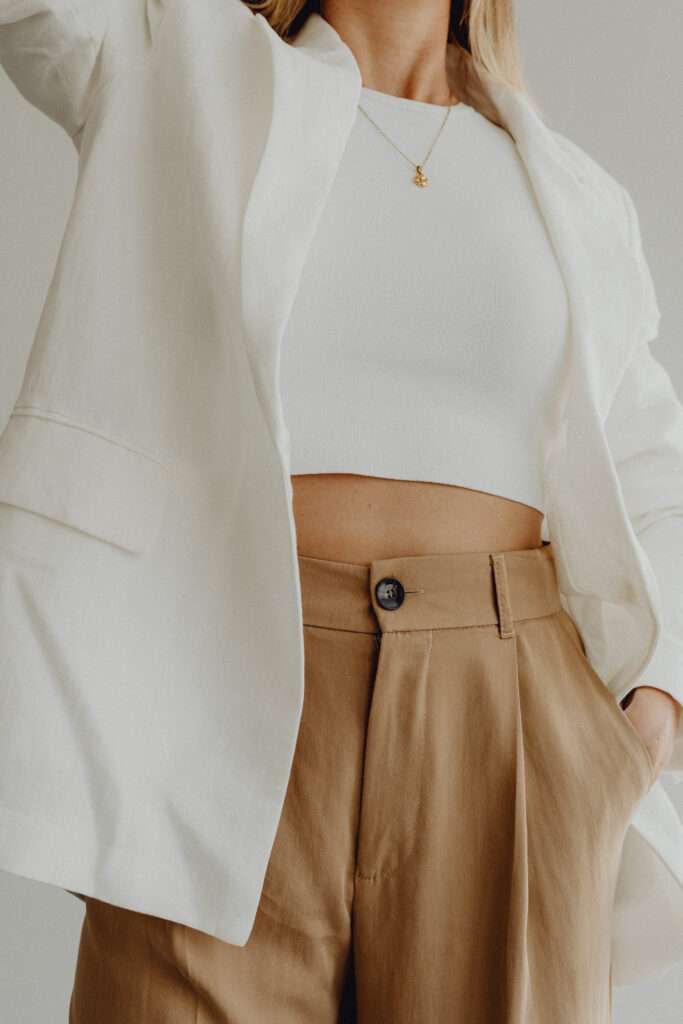 How to reinvent yourself physically through style. A close up image of a woman wearing a white blazer, white crop top, and brown trousers.