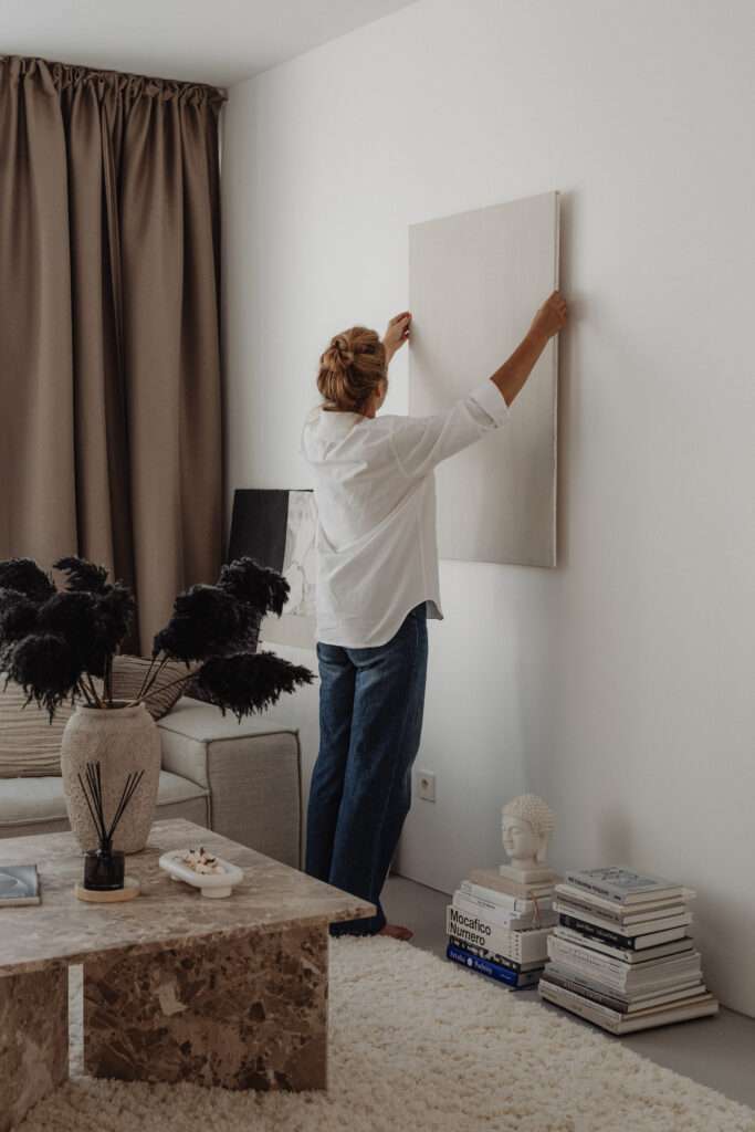 Reinvent yourself physically by creating an inspiring environment. Woman hanging up a canvas painting on the wall