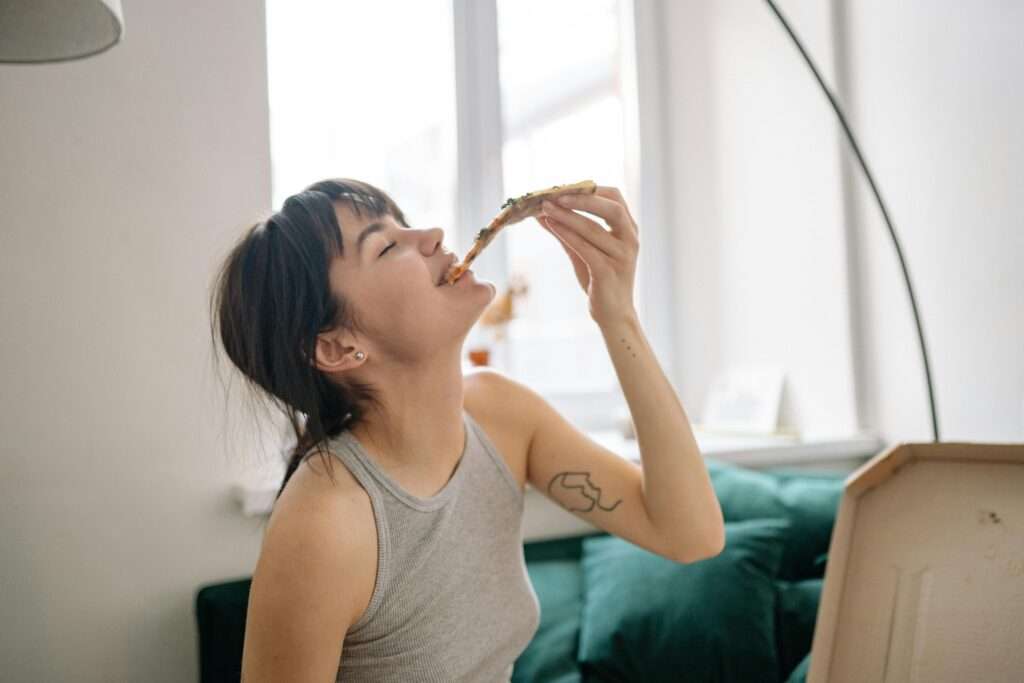 Repairing your relationship with food by enjoying it. A woman eating a slice of pizza.