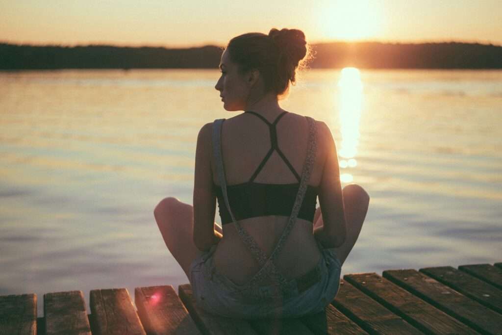 A woman sitting in the front of a lake during sunset.