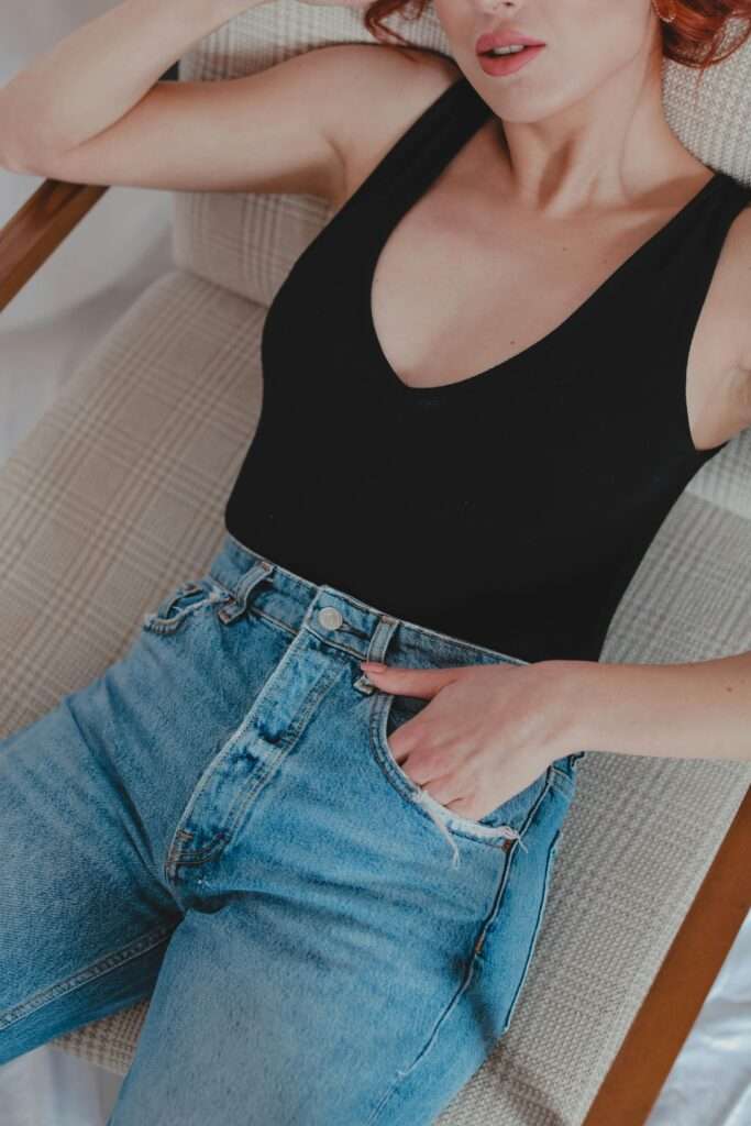 A woman sitting on a chair, wearing a black bodysuit and high waist jeans