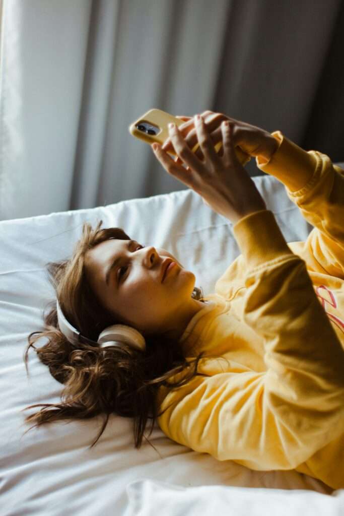 Woman lying on bed with headphones in listening to music