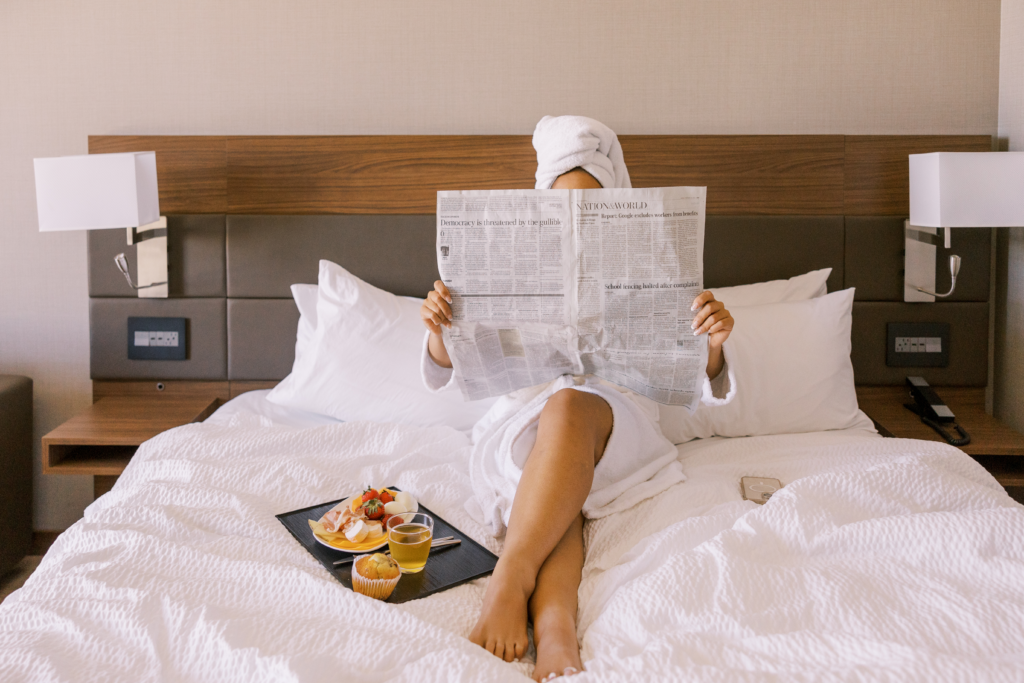 A woman in a hotel room having breakfast and reading a newspaper