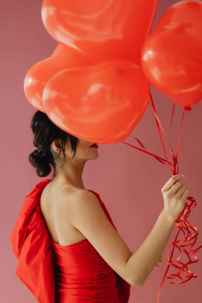 A woman taking a photo while holding heart shaped balloons