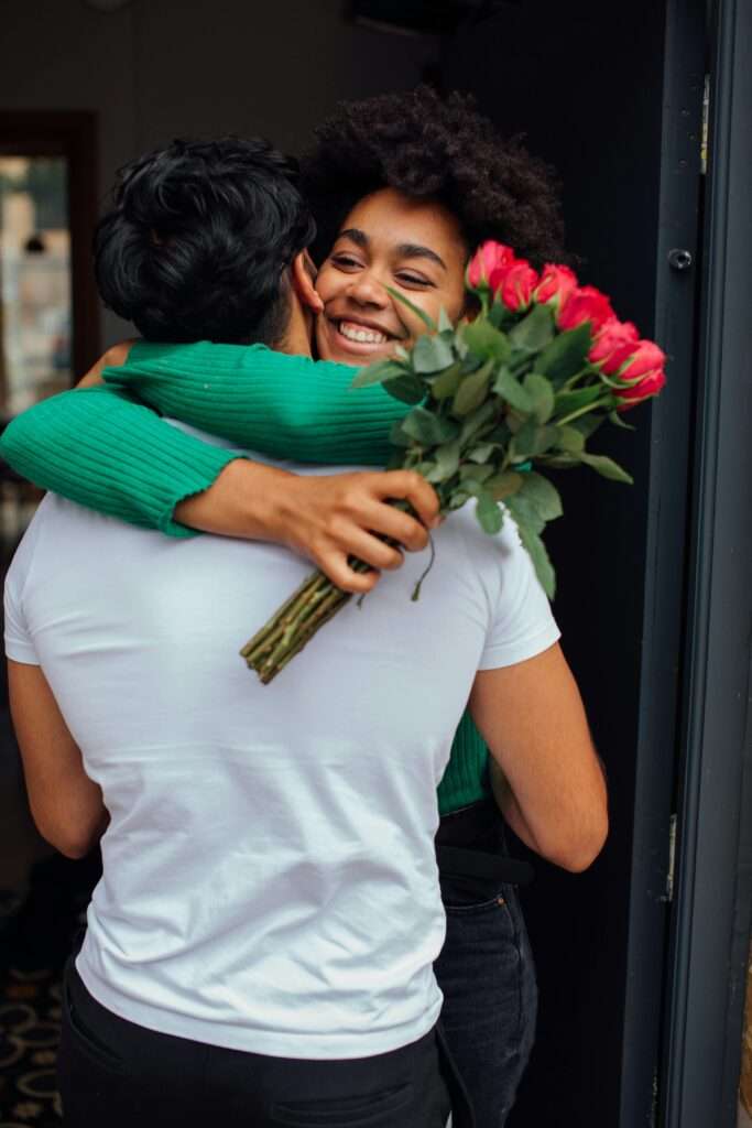 An image of a woman hugging a man with flowers in her hand.
