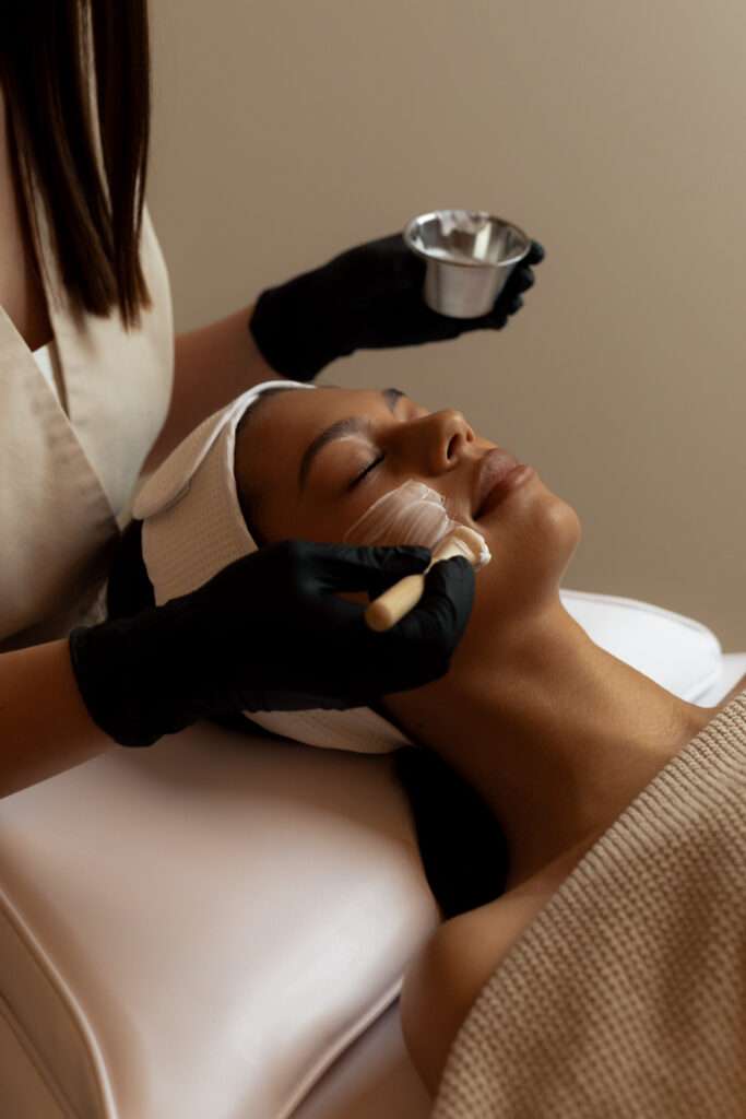 A close up image of an esthetician putting a facial mask on client's face.