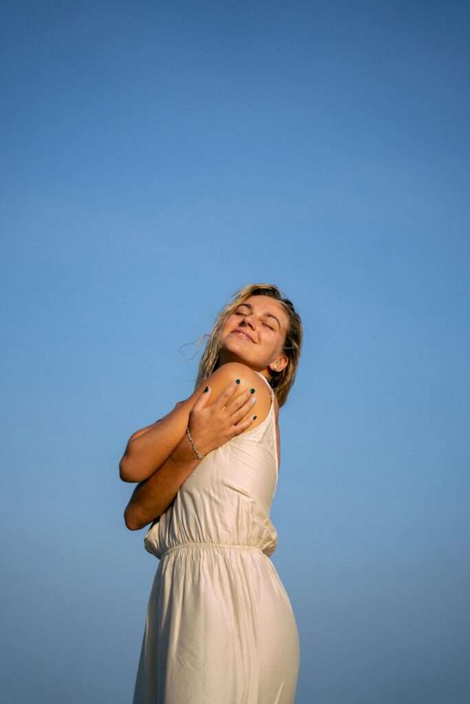 An image of a woman hugging herself while smiling.