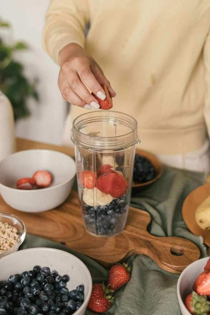 A close up image of a woman's hand putting fruit in a blender.