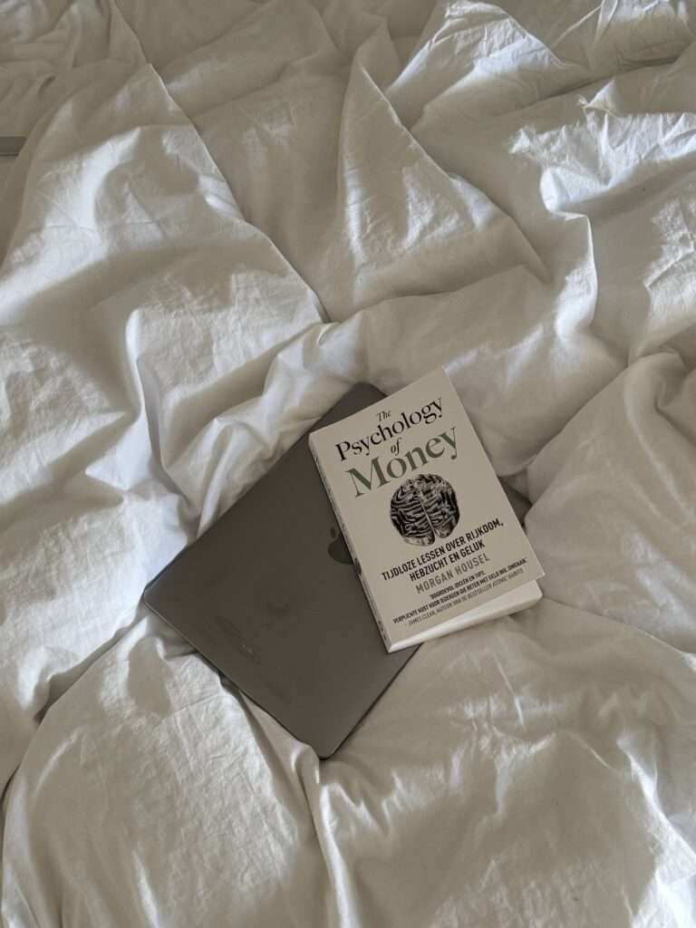 Image of The Psychology of Money by Morgan Housel and a Macbook on the bed.