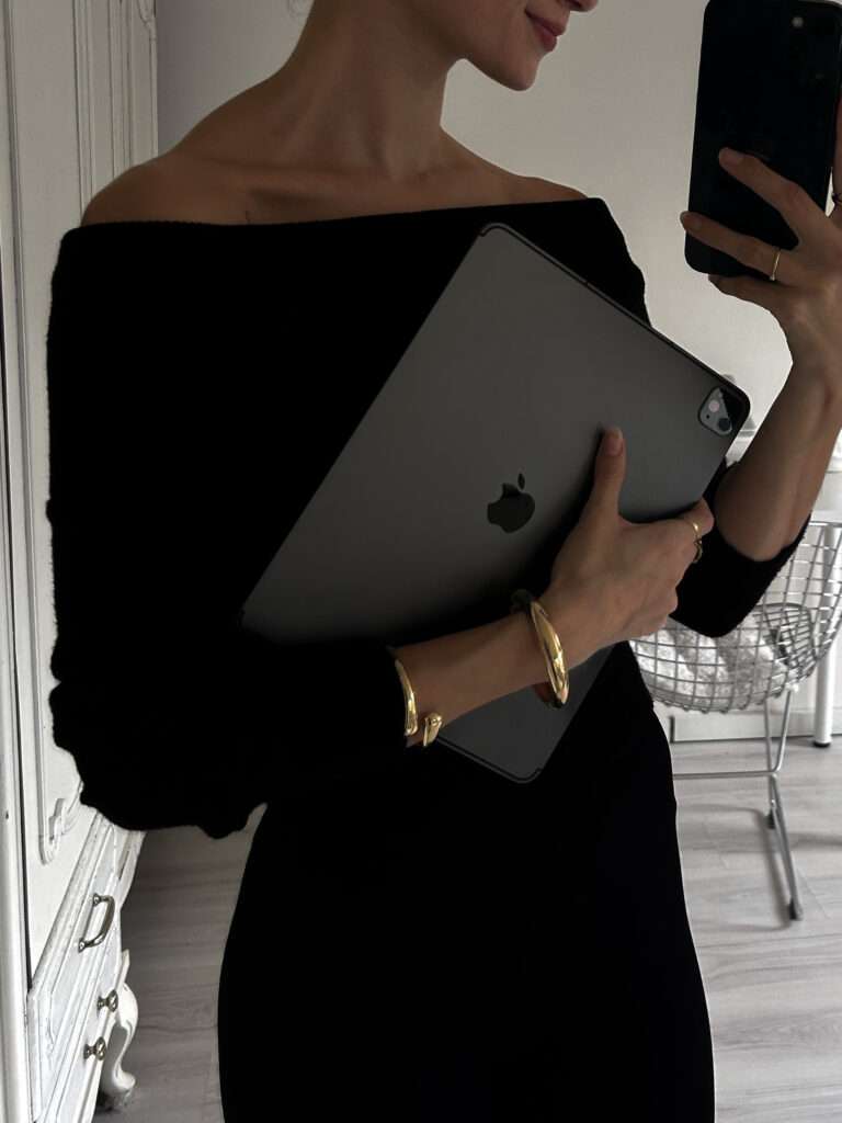 Image of a woman taking a picture on her phone whilst standing in a mirror and holding her ipad.