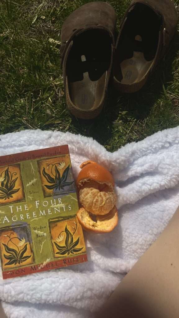 Image of The Four Agreement by Don Miguel Ruiz book and oranges on a white blanket.