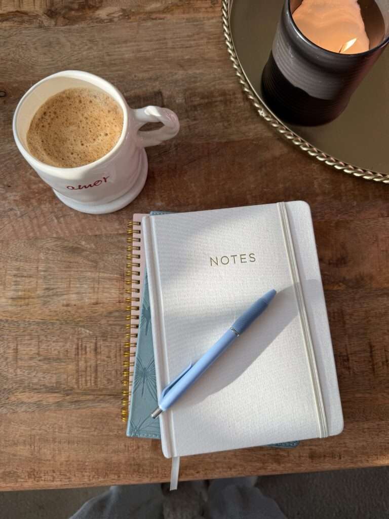 Image of notebooks, a cup of coffee, and a candle on a wooden table.