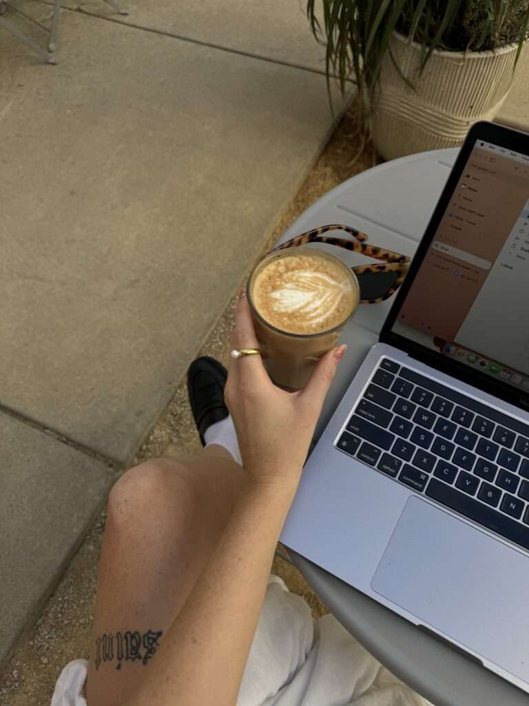 A close-up image of a woman sitting, drinking coffee and on macbook.