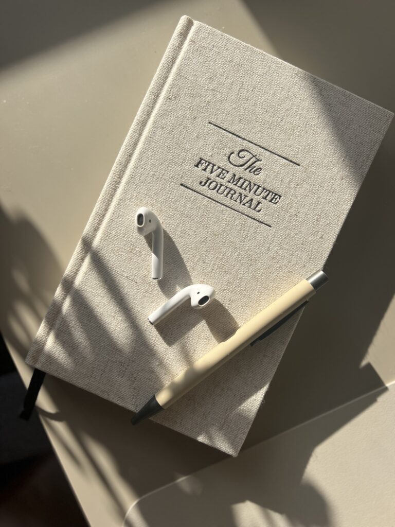 Image of "The Five-Minute Journal", headphones, and a pen lying on a table.
