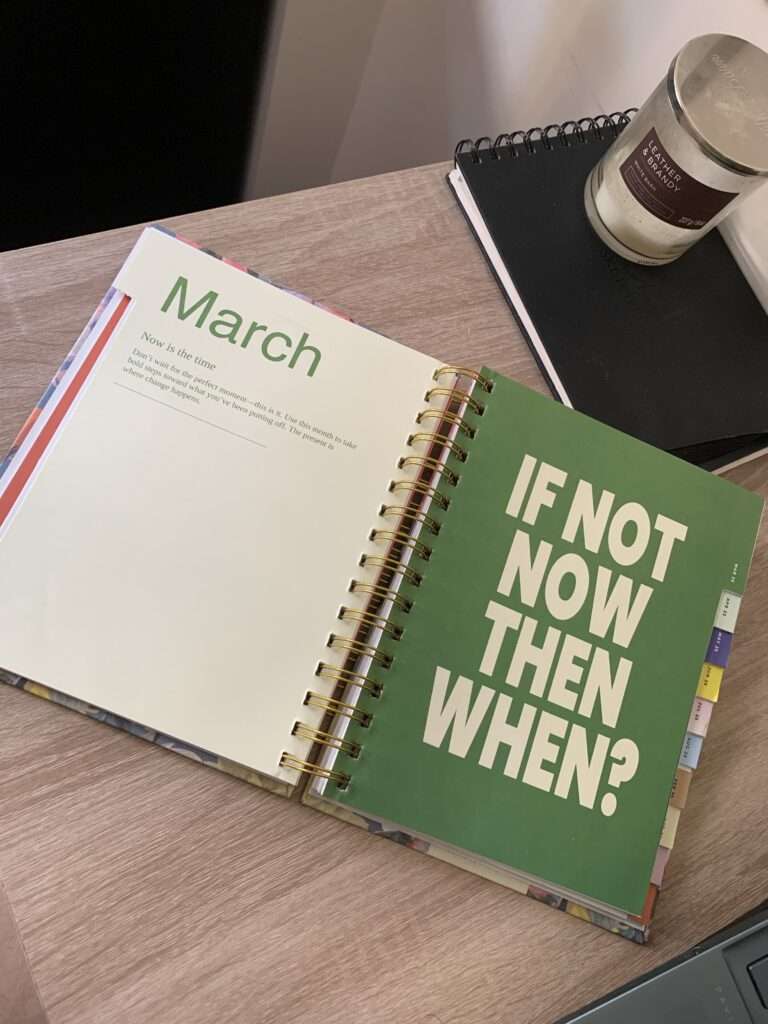 An image of a planner, a black notebook, and candle on a wooden desk.