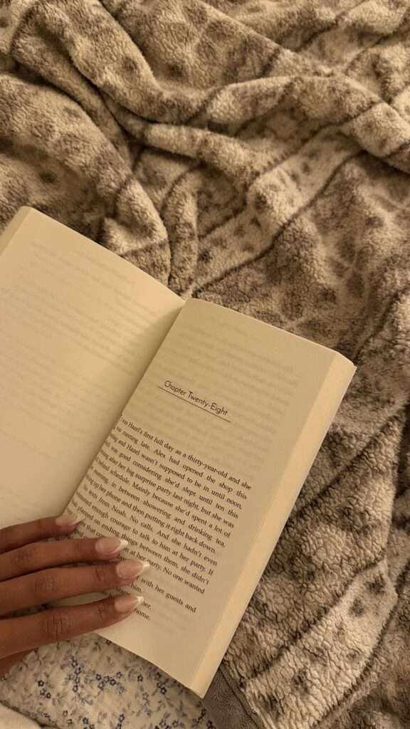 A close-up image of a novel, woman fingers, and blanket.