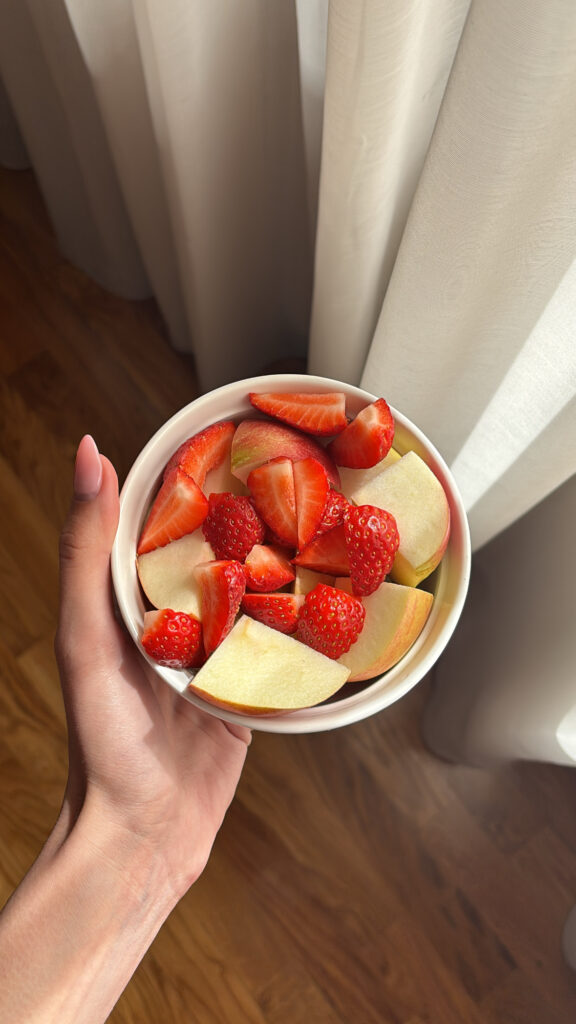 Image of a close-up picture of a woman holding a bowl of dice strawberries and apples.