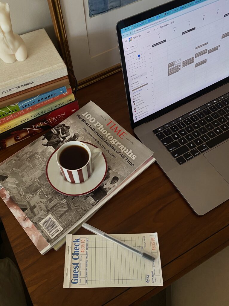 Image of a laptop, coffee cup, magazines, pen, and notepad on a desk.
