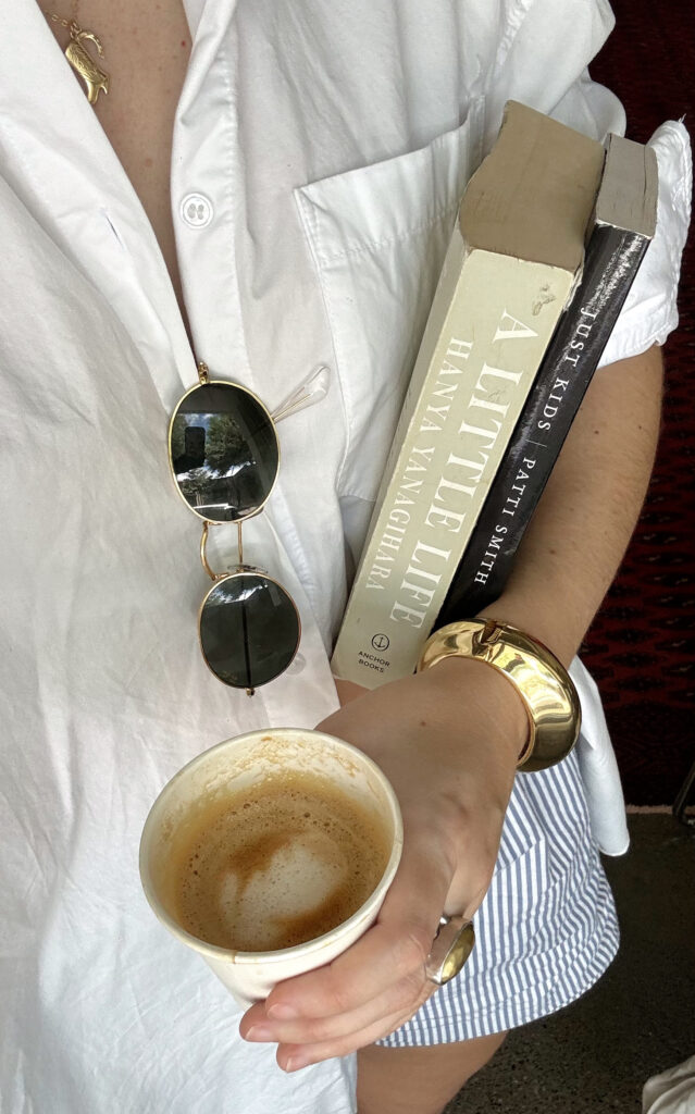 An image of a woman taking a selfie holding books and coffee.