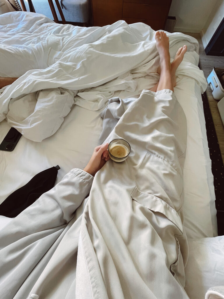 Image of a woman holding a mug of coffee whilst sitting in bed.