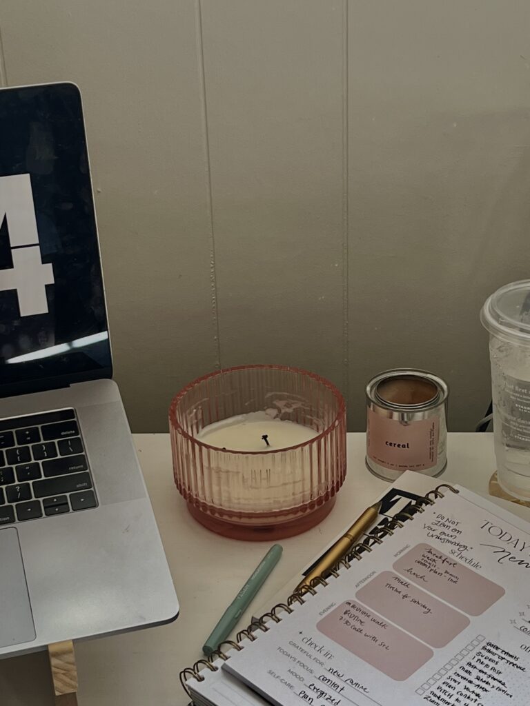 Image of a laptop, candle, and notebook on a desk.